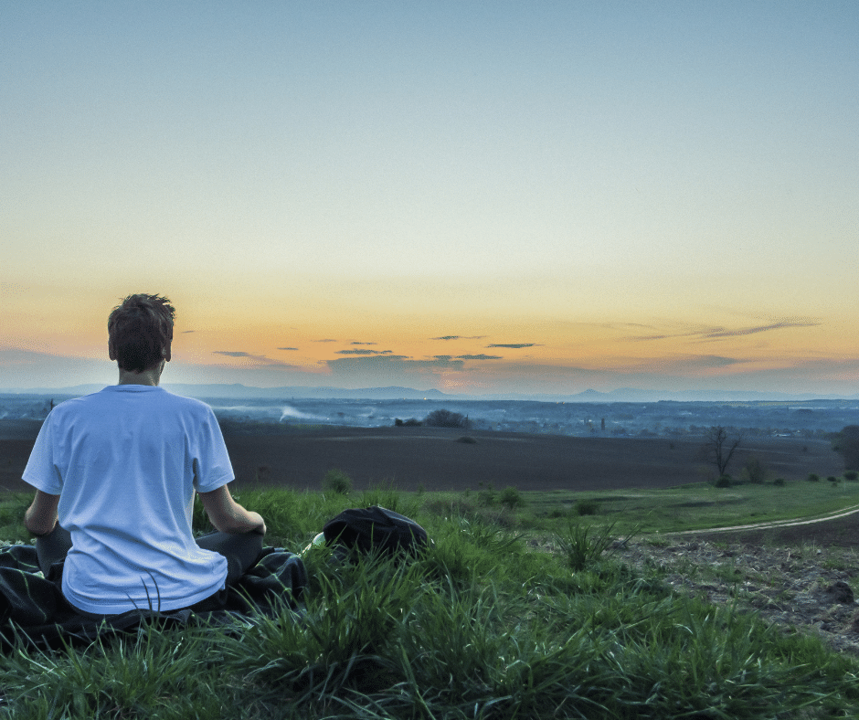 Man sitting , meditating during sunset by a mountain range!