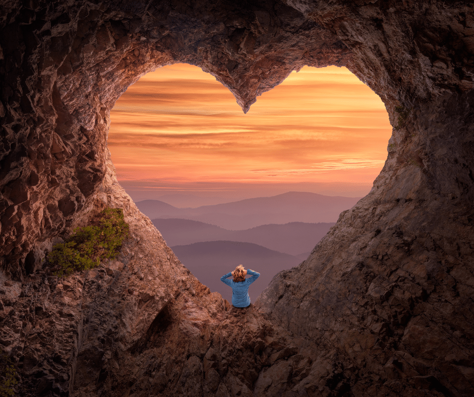 Woman looking through a heart shaped look out overlooking a red and blue tinted mountain horizon. 